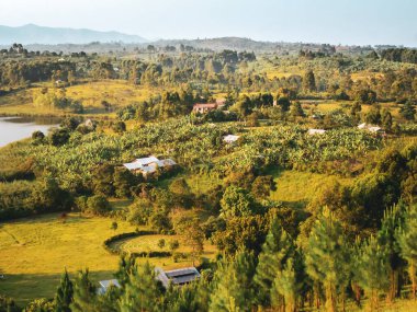 Yeşil tarlaların, ağaçlar arasında dağılmış evlerin ve berrak bir gökyüzünün altında sakin ve huzurlu bir atmosferi çağrıştıran uzak bir sıradağların bulunduğu pitoresk bir kırsal bölge..
