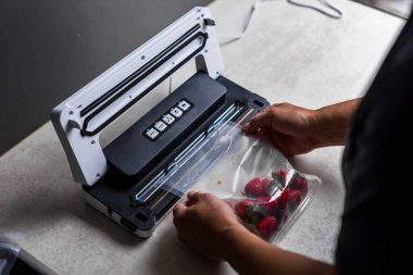 Bir adamın eli vakum makinesi kullanarak çilekleri plastik poşetlere boşaltıyor. - Evet. Yüksek kalite fotoğraf