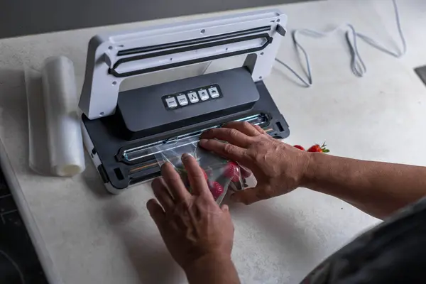 stock image a mans hand is using a vacuum machine to vacuum pack strawberries into plastic bags. . High quality photo