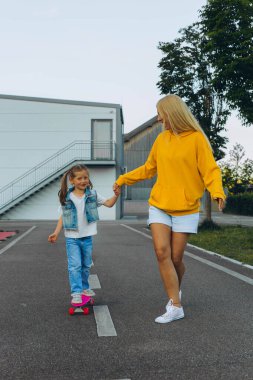 Aktif küçük kız ve anne kaykayla eğleniyor. Anne kızını kaykay için eğitiyor. - Evet. Yüksek kalite fotoğraf