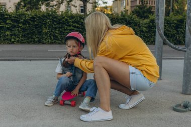 Anne kızına kask takıp kaykay sürmesi için yardım ediyor. Yüksek kalite fotoğraf