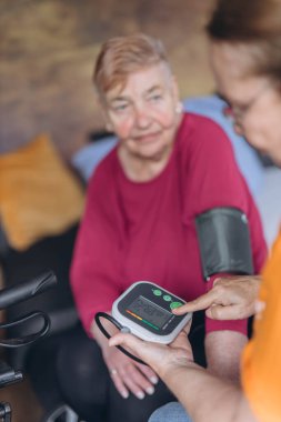 Yaşlı bir kadın yatağa oturur ve kan basıncını bir kadın gönüllü ölçer. Yüksek kalite fotoğraf