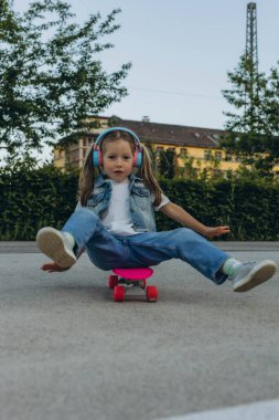 kid girl playing surf skate or skateboard in headphones. High quality photo clipart