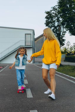 Anne kızına kask takıp kaykay sürmesi için yardım ediyor. Yüksek kalite fotoğraf