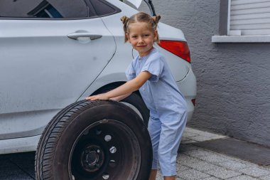 Sevimli küçük kız sıcak bir günde babasının aile arabasının tekerleğini değiştirmesine yardım ediyor. Yüksek kalite fotoğraf