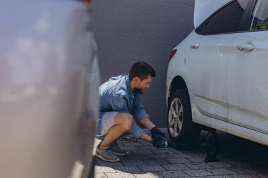 Lastik değiştirme işleminde vida sökücü fındıklı genç adam yolda lastiği değiştirirken ingiliz anahtarı kullanıyor. Yüksek kalite fotoğraf