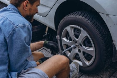 Lastik değiştirme işleminde vida sökücü fındıklı genç adam yolda lastiği değiştirirken ingiliz anahtarı kullanıyor. Yüksek kalite fotoğraf