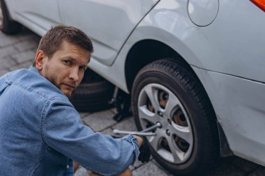 Lastik değiştirme işleminde vida sökücü fındıklı genç adam yolda lastiği değiştirirken ingiliz anahtarı kullanıyor. Yüksek kalite fotoğraf