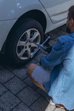 Lastik değiştirme işleminde vida sökücü fındıklı genç adam yolda lastiği değiştirirken ingiliz anahtarı kullanıyor. Yüksek kalite fotoğraf