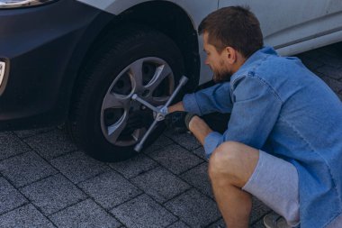 Lastik değiştirme işleminde vida sökücü fındıklı genç adam yolda lastiği değiştirirken ingiliz anahtarı kullanıyor. Yüksek kalite fotoğraf