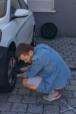 Lastik değiştirme işleminde vida sökücü fındıklı genç adam yolda lastiği değiştirirken ingiliz anahtarı kullanıyor. Yüksek kalite fotoğraf
