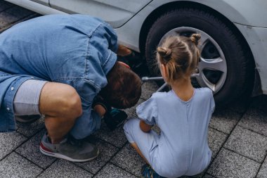 Sevimli küçük kız sıcak bir günde babasının aile arabasının tekerleğini değiştirmesine yardım ediyor. Yüksek kalite fotoğraf