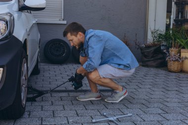 Lastik değiştirme işleminde vida sökücü fındıklı genç adam yolda lastiği değiştirirken ingiliz anahtarı kullanıyor. Yüksek kalite fotoğraf