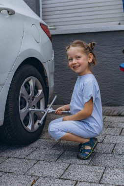 Sevimli küçük kız sıcak bir günde babasının aile arabasının tekerleğini değiştirmesine yardım ediyor. Yüksek kalite fotoğraf