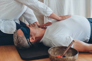 Gözü bağlı bir şekilde mindere uzanmış bir adam, bir kadın koç gibi davranırken, nefes egzersizleri yapıyor, ona yardım ediyor. Yüksek kalite fotoğraf