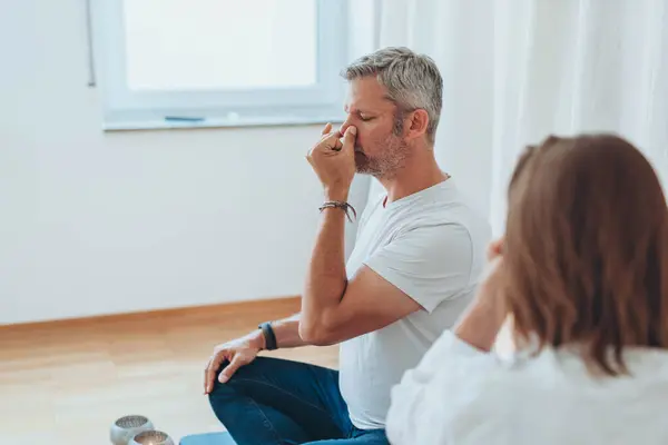 Stock image A man sitting in lotus position and a woman practicing alternate nostril breathing exercises during a meditation session. High quality photo