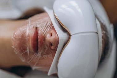 Genç bir kadın, sağlık ve sağlık hizmetlerini ön plana çıkaran bir cihazla göz masajı yaptırıyor. Yüksek kalite fotoğraf