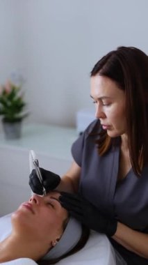 Tıp eldivenli profesyonel dermatolog güzellik salonunda bir kadına mikro cilt bakımı yapıyor.