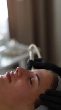 Tıp eldivenli profesyonel dermatolog güzellik salonunda bir kadına mikro cilt bakımı yapıyor.