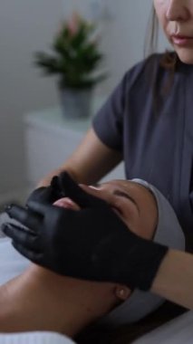 Kozmetik uzmanı, güzellik salonunda cilt bakımına odaklanmış genç bir kadının cildini temizliyor.
