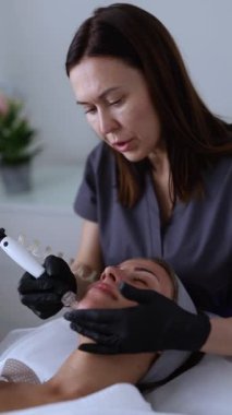 Tıp eldivenli profesyonel dermatolog güzellik salonunda bir kadına mikro cilt bakımı yapıyor.