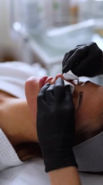 Bir kozmetolog profesyonel cilt bakımı sırasında genç bir kadının cildini dikkatlice temizler..