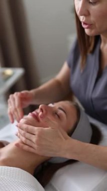Kozmetik uzmanı, güzellik salonunda cilt bakımına odaklanmış genç bir kadının cildini temizliyor.