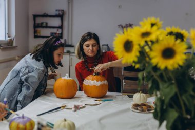 Çocuklar ve yetişkinler Cadılar Bayramı için balkabağı boyuyor, eğlenceli ve yaratıcı aktivitelerin tadını çıkarıyorlar. Yüksek kalite fotoğraf