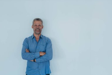 Mavi gömlekli genç bir profesyonel, karşısında duruyor, beyaz arka planı ve kolları çapraz. Yüksek kalite fotoğraf