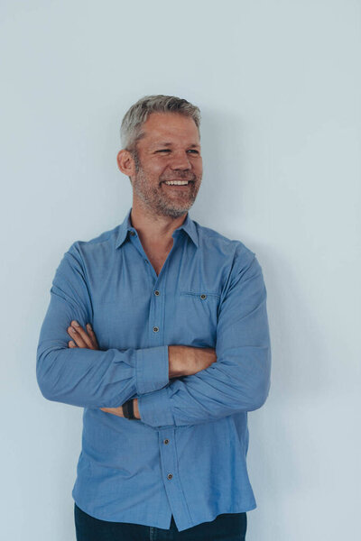 Молодой профессионал в синей рубашке, стоящий напротив, белый фон со скрещенными руками. Высокое качество фото