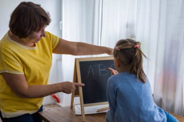 Büyükannesi yanında öğretmenlik yaparken 5 yaşında bir kız tahtaya mektup yazıyor. Yüksek kalite fotoğraf