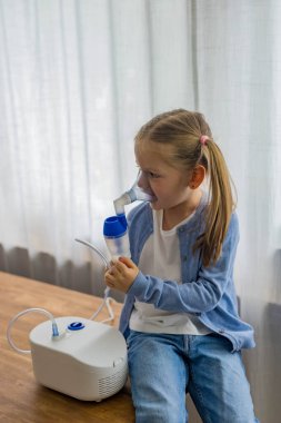 Evde, 5 yaşındaki bir kız nebulizatörle nefes alıp veriyor, solunum terapisine odaklanıyor. Yüksek kalite fotoğraf