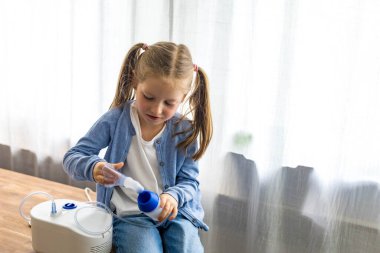 Evde, 5 yaşındaki bir kız nebulizatörle nefes alıp veriyor, solunum terapisine odaklanıyor. Yüksek kalite fotoğraf