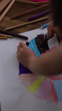 5 yaşındaki bir kız renkli kalemlerle resim çiziyor, kendi çizimlerini yapmaya odaklanıyor..