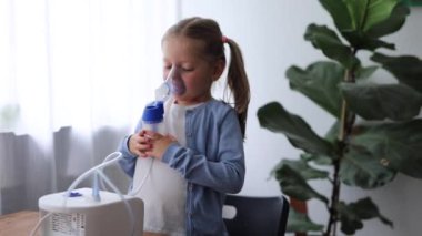 Evde 5 yaşında bir kız çocuğu nebulizör kullanıyor. Solunum sağlığına yardımcı olmak için derin nefes alıyor.