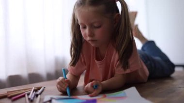 5 yaşındaki bir kız renkli kalemlerle resim çiziyor, kendi çizimlerini yapmaya odaklanıyor..