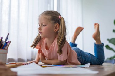 Gülen ve eğlenen 5 yaşındaki kız çizimlerini parlak kalemlerle dolu masada yapıyor. Yüksek kalite fotoğraf