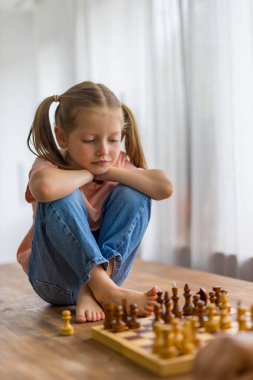 5 yaşındaki bir kız, bir sonraki hamlesini dikkatlice planlarken dikkatle odaklanarak küçük bir satranç takımıyla oynuyor. Yüksek kalite fotoğraf