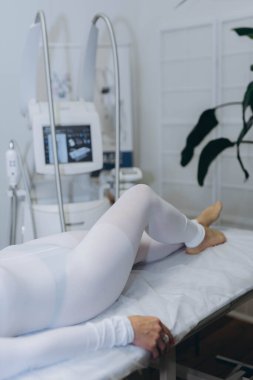 Bir güzellik kliniğinde LPG masajı için beyaz takım elbiseli bir kanepede yatan genç bir kadın. Yüksek kalite fotoğraf