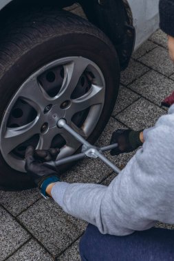 Delikanlı yolda lastik değiştiriyor, vidaları sökmek için İngiliz anahtarı kullanıyor. Yüksek kalite fotoğraf