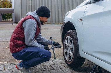 Adam arabasının lastiğini ingiliz anahtarıyla değiştiriyor, yerine kış lastiklerini takıyor. Yüksek kalite fotoğraf