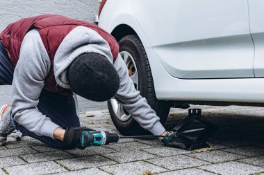 Adam, soğuk havaya hazırlanmak için ingiliz anahtarı kullanarak arabasının lastiklerini kış lastikleriyle değiştiriyor. Yüksek kalite fotoğraf
