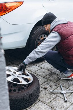Adam, soğuk havaya hazırlanmak için ingiliz anahtarı kullanarak arabasının lastiklerini kış lastikleriyle değiştiriyor. Yüksek kalite fotoğraf