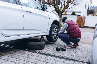 Adam, soğuk havaya hazırlanmak için ingiliz anahtarı kullanarak arabasının lastiklerini kış lastikleriyle değiştiriyor. Yüksek kalite fotoğraf