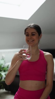 Pembe elbiseli spor bir kadın elinde bir bardak su tutuyor, sağlık ve zindeliği temsil ediyor.
