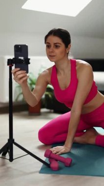 Pembe spor takım elbiseli bir kadın akıllı telefonuyla online antrenman yapıyor. Yüksek kaliteli FullHD görüntüler