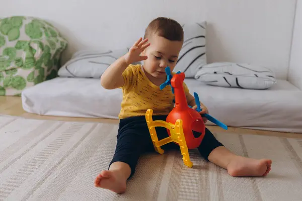 Bebek yerde oturuyor, kırmızı bir helikopterle oynuyor, eğlence ve keşfin tadını çıkarıyor. Yüksek kalite fotoğraf
