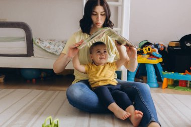 Anne ve iki yaşındaki oğlu çocuk odasında oynuyorlar, anneliği ve bakımı sembolize ediyorlar. Yüksek kalite fotoğraf