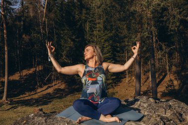 Gün batımında bir kayanın tepesinde meditasyon yapan ve yoga yapan bir kadın, sağlığını, farkındalığını ve çevre dostu hayatını kucaklıyor. Yüksek kalite fotoğraf