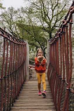 Asılı bir halat köprüsünde koşan genç bir kız, neşeli bir açık hava ortamında enerji ve macera dolu. Yüksek kalite fotoğraf